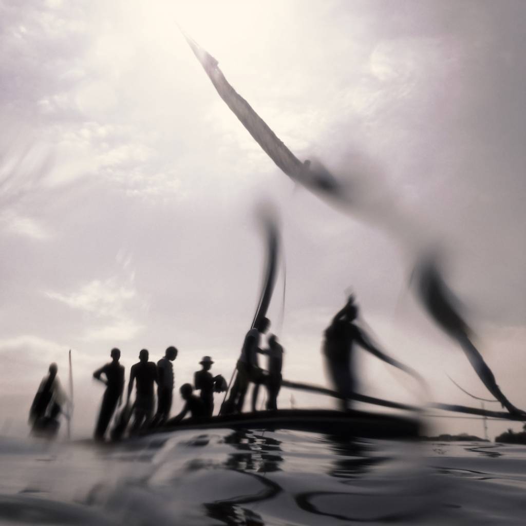 Imagem preto e branco onde a silhueta de pessoas em cima de um barco é distorcida.