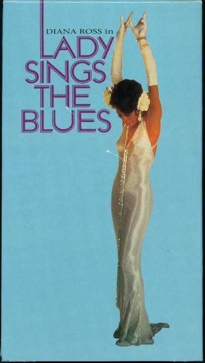 Diana Ross em um vestido longo prateado, com luvas brancas e flores no cabelo, bra&ccedil;os erguidos e cabe&ccedil;a baixa, sobre fundo azul claro. O t&iacute;tulo DIANA ROSS in LADY SINGS THE BLUES aparece em roxo na lateral esquerda